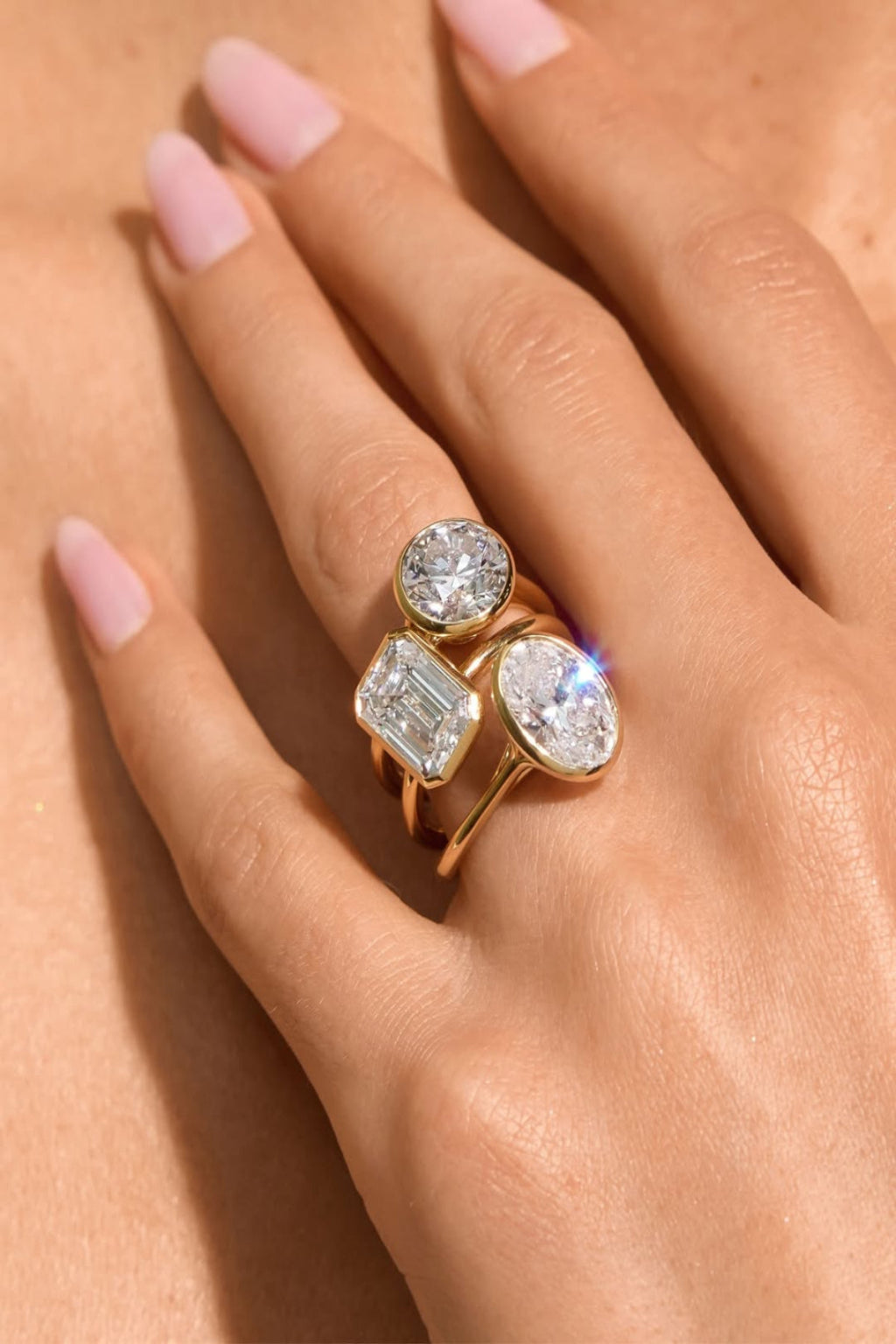 Hand wearing a gold ring with three diamond stones on a neutral background